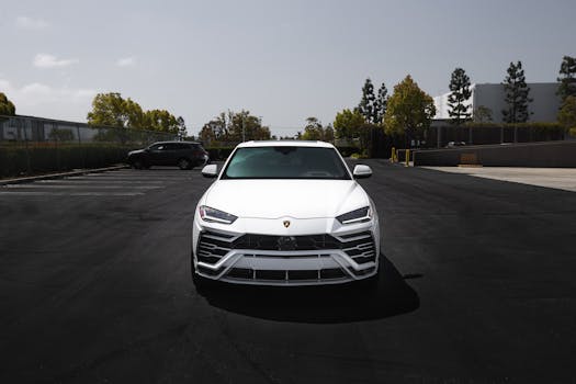 Front view of a white Lamborghini Urus parked in a spacious parking lot under clear skies.