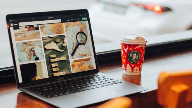A stylish workspace featuring a laptop displaying travel images and a festive coffee cup on a wooden table.