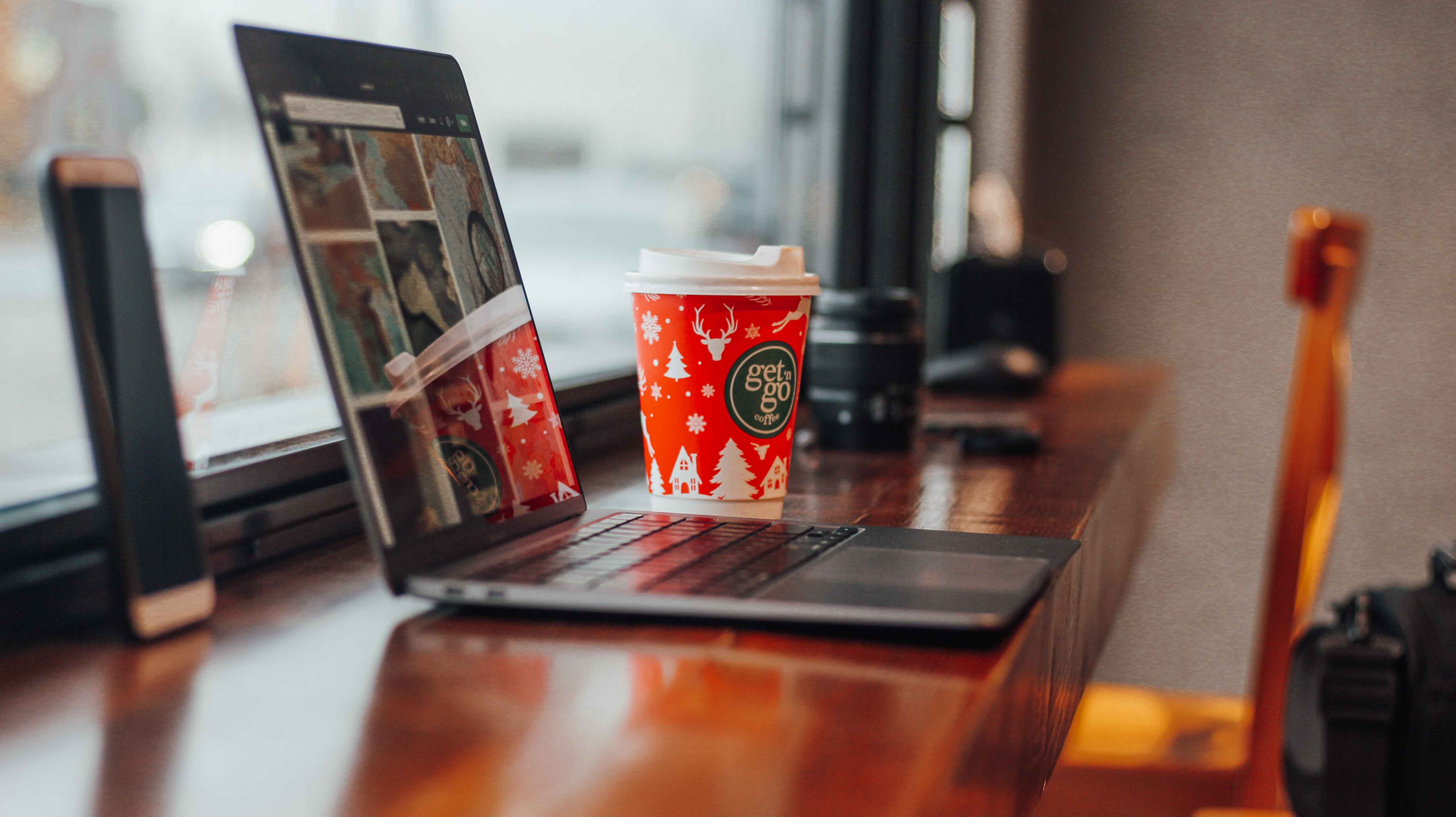 Warm indoor scene with a laptop and Christmas-themed coffee cup on a wooden table.