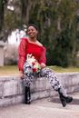 Smiling Woman with Short African Hairstyle Sitting on Low Wall in Park 