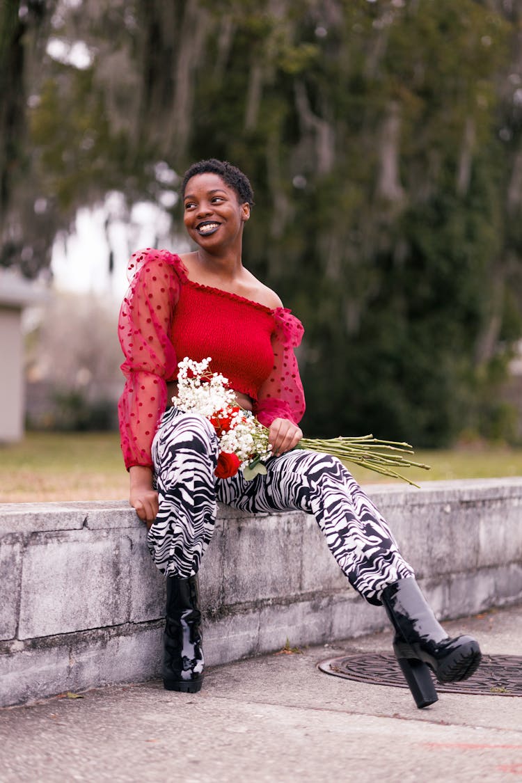 Smiling Woman With Short African Hairstyle Sitting On Low Wall In Park 