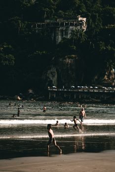 People enjoying a day at the beach with forested cliffs and waves.