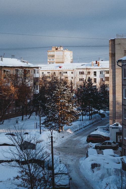 Free A winter street scene with snow-covered buildings and trees under a gloomy sky. Stock Photo