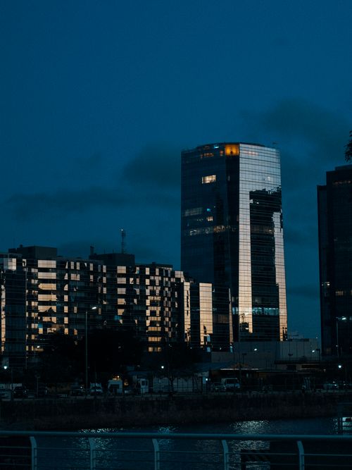 Free Reflective skyscrapers stand tall against a night sky along a waterfront. Stock Photo