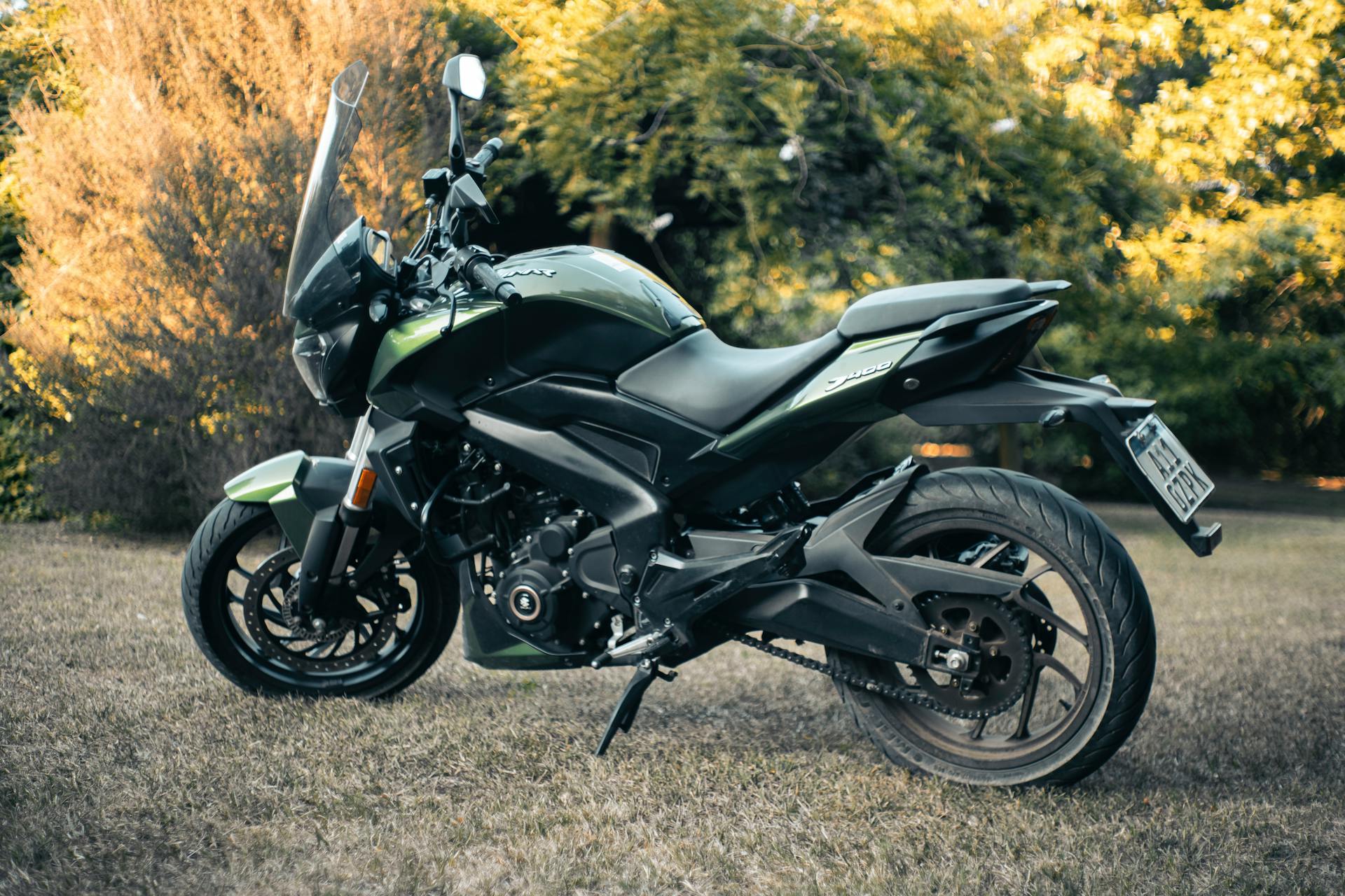 A sleek green Bajaj Dominar 400 motorcycle parked on grass, surrounded by nature.