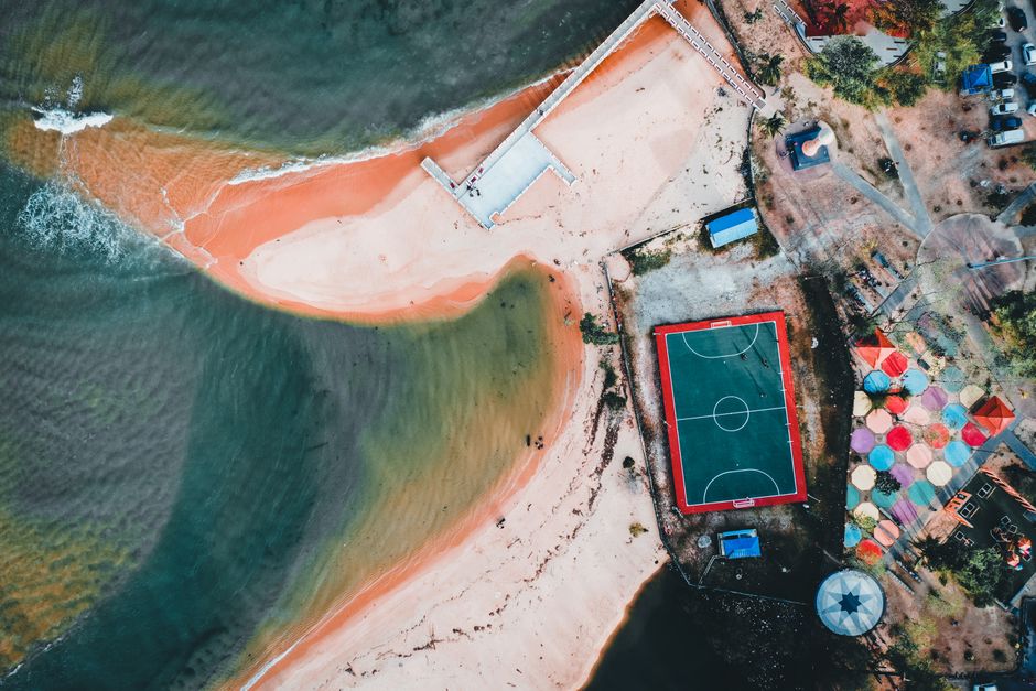 Stunning aerial shot of a beachside football court and colorful umbrellas.