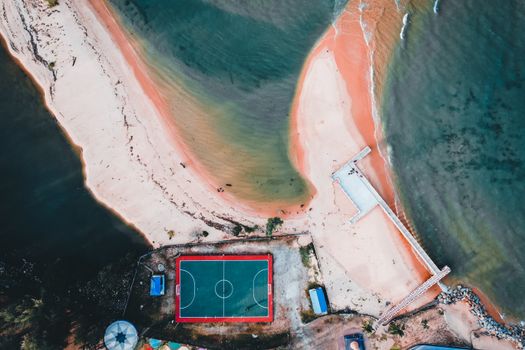 A stunning aerial view of a football pitch near a vibrant beach shoreline.
