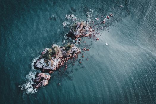 Stunning aerial shot of a rocky island surrounded by turquoise sea, showcasing nature's beauty.