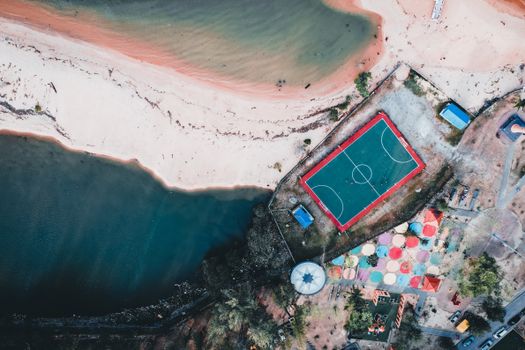 Drone shot of a beachside sports court near colorful tents and calm waters.