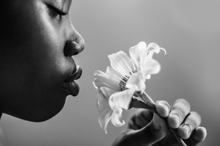 Close-up black and white photo of a woman with eyes closed, smelling a delicate white flower.