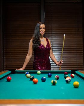 Young woman in a sequined dress playing billiards indoors with a confident smile.