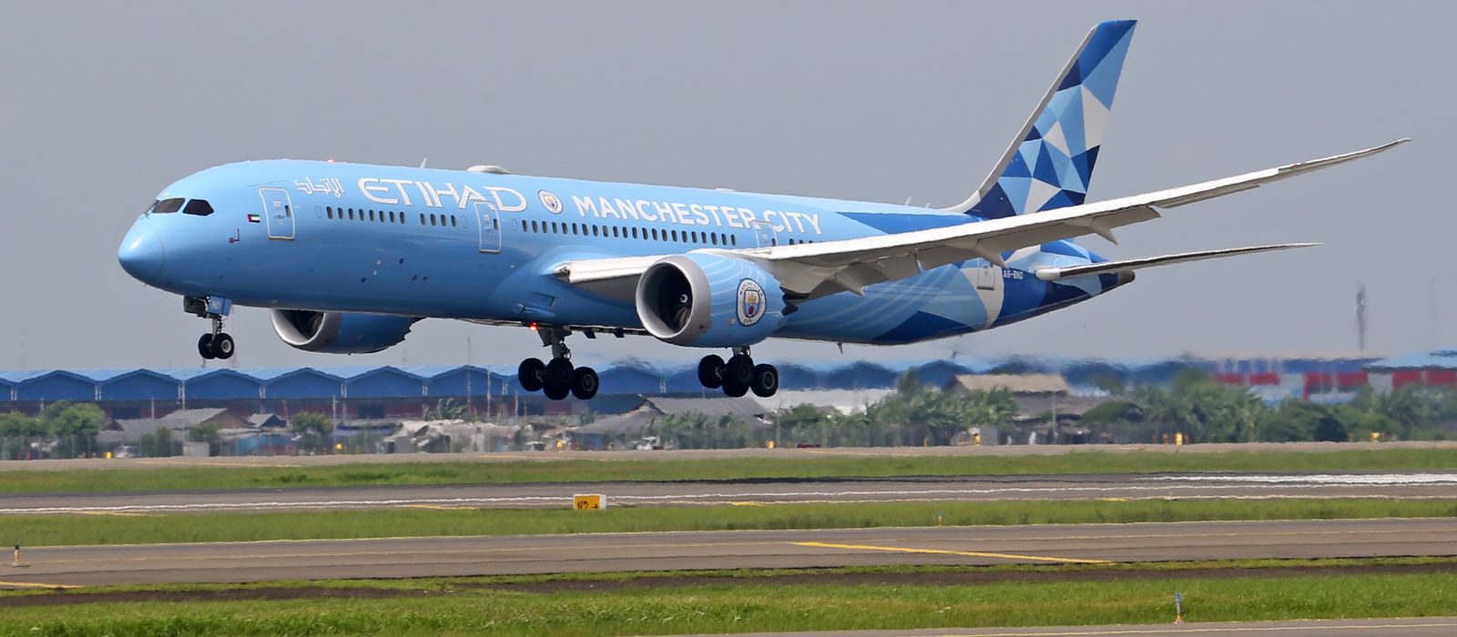 Etihad Airways aircraft with Manchester City branding landing on a runway, showcasing vivid livery.