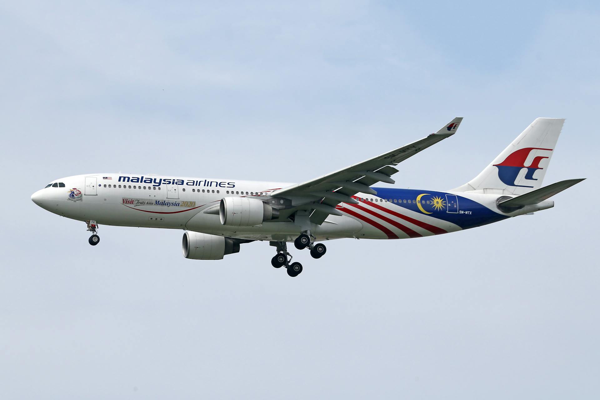 Malaysia Airlines Airbus showcasing national flag colors during flight with landing gear down.