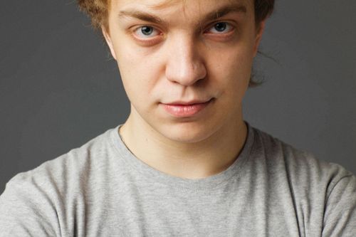 Free Expressive close-up portrait of a young man with a neutral facial expression against a gray backdrop. Stock Photo