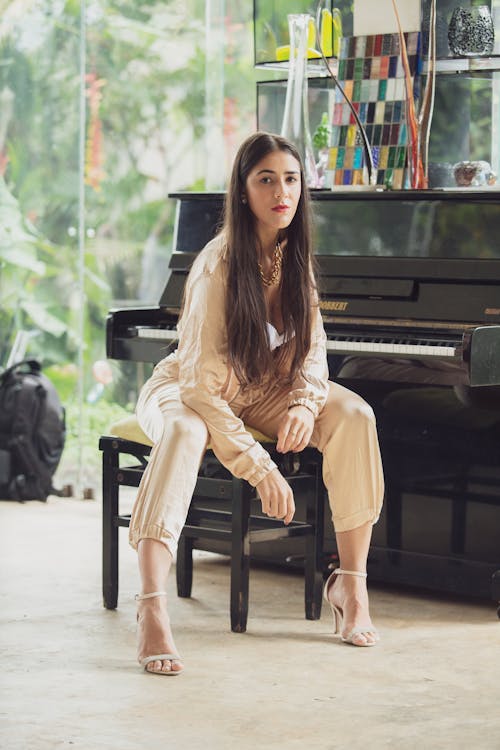 Free Woman in Beige Outfit Sitting Beside a Piano Stock Photo