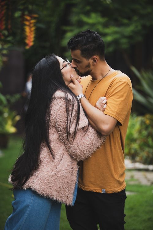 Free A loving couple shares a tender kiss in a lush green garden setting, displaying affection and joy. Stock Photo