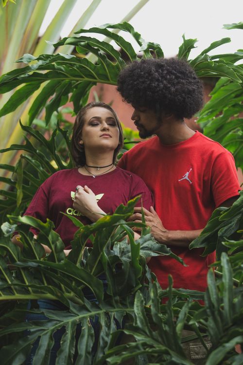 Free A young couple embracing amidst vibrant green leaves, symbolizing love and nature connection. Stock Photo