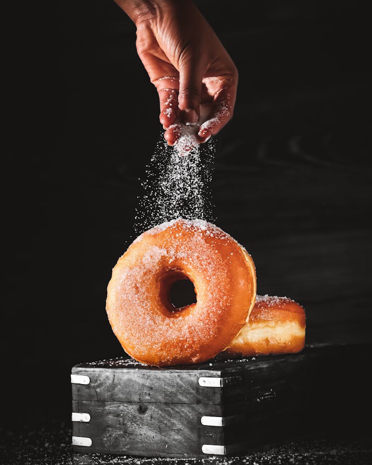 Person Sprinkling Donuts With Sugar