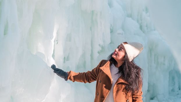 A woman in a winter coat admires beautiful ice formations outdoors on a sunny winter day.