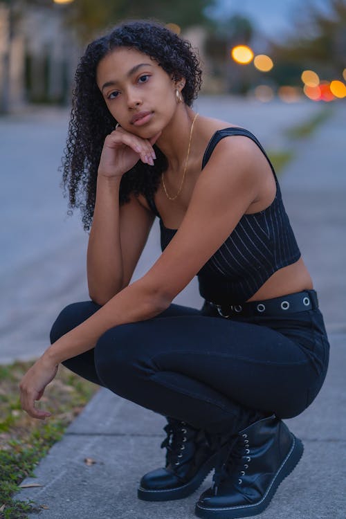 Photo of a Woman in Black Clothes Crouching on the Side of the Road