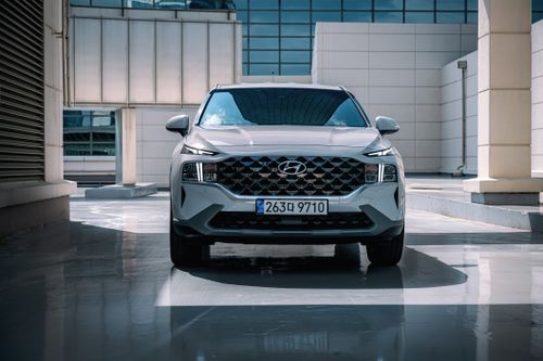 Free Front view of a white Hyundai Santa Fe SUV parked in an urban setting with sleek architecture. Stock Photo