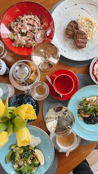 Top-down view of a diverse meal setting featuring steak, salads, and drinks on a wooden table.