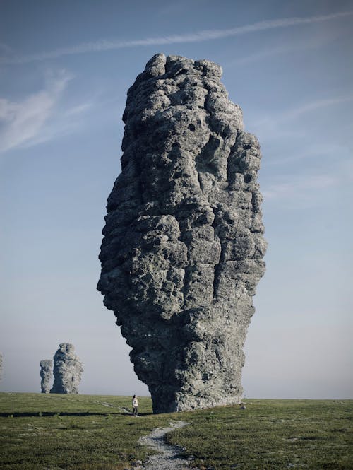 A Person Standing Beside Gray Rock Formation on Green Grass Field