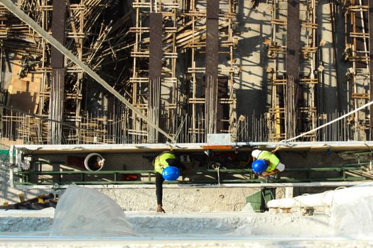 Top view of two construction workers on a scaffold with wooden framework below.
