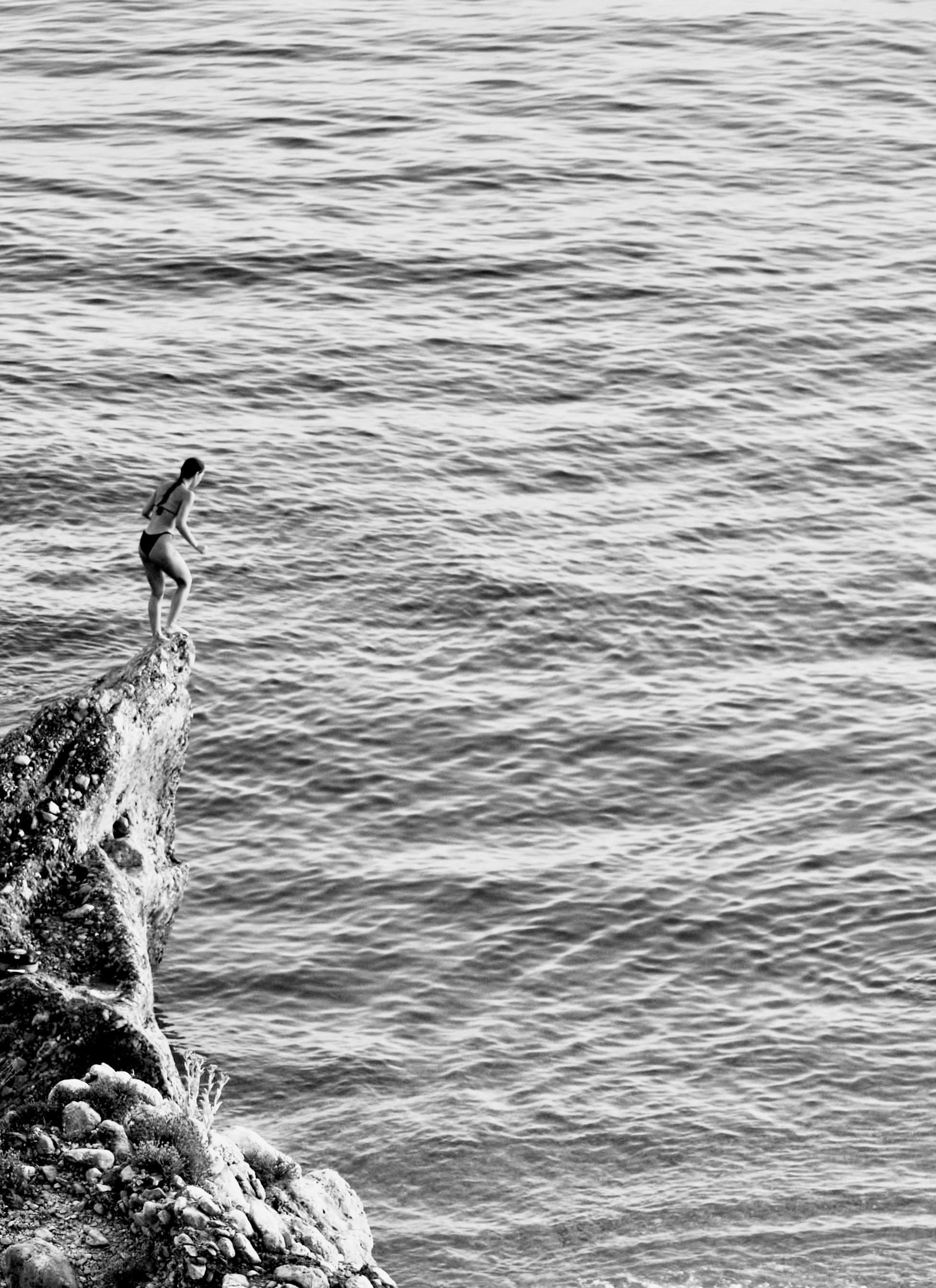 Woman poised to dive from a rocky cliff into the ocean at Drymades, Albania.
