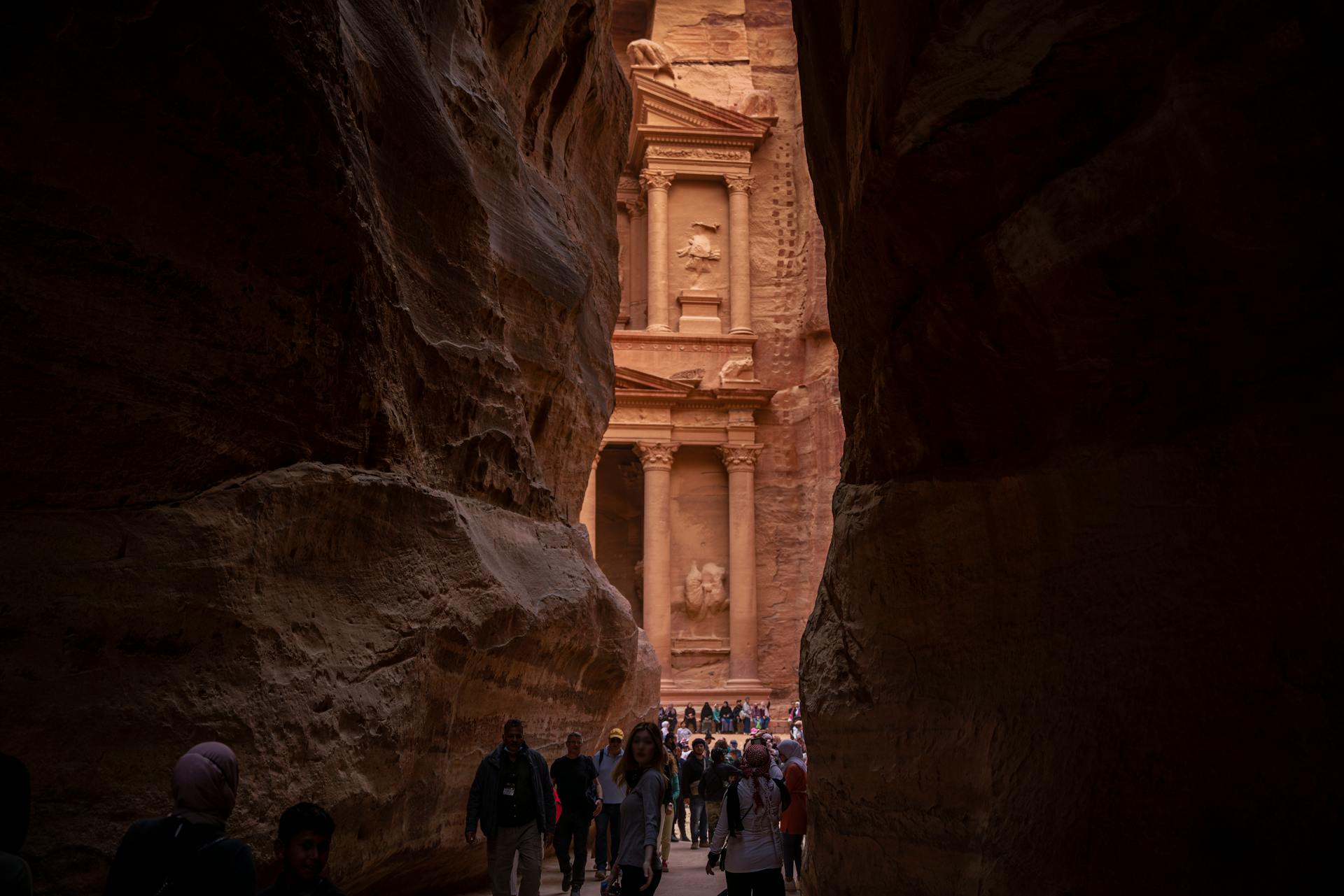 Tourists walking towards the famous Treasury in Petra through a narrow gorge.