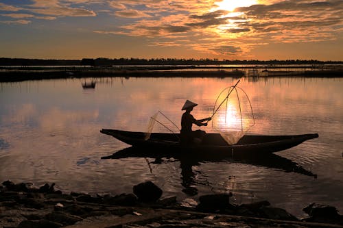 Man Fishing on Boat on Lake during Sunset