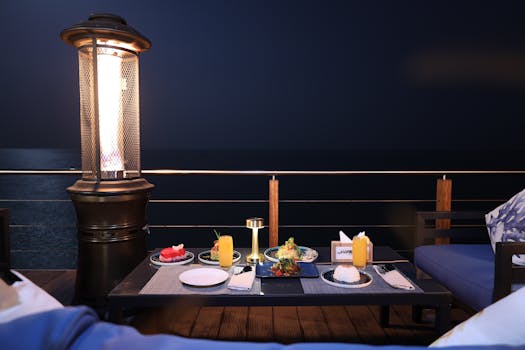A romantic outdoor dinner setup with a sea view under night skies, lit by lamps.