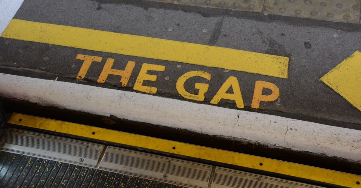 Close-up of 'Mind the Gap' warning sign on station platform edge, focusing on safety.