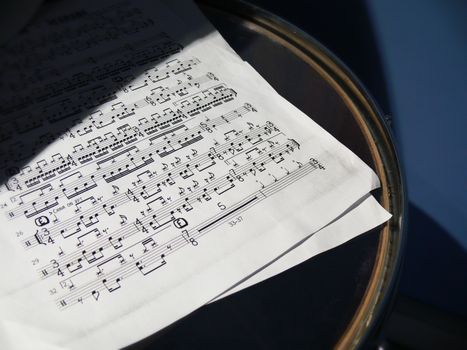 A detailed view of sheet music placed on a drum under soft sunlight, creating artistic shadows.