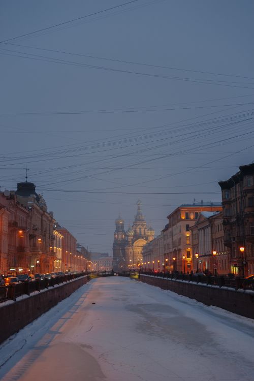 Free Snowy city street with a glowing church at twilight. Serene winter scene. Stock Photo