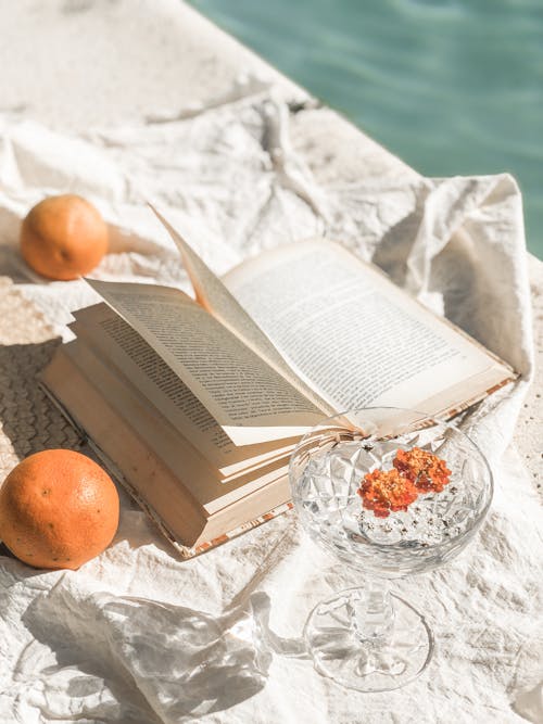 AN Open Book Beside Glass with Water and Tangerines on a White Surfacae