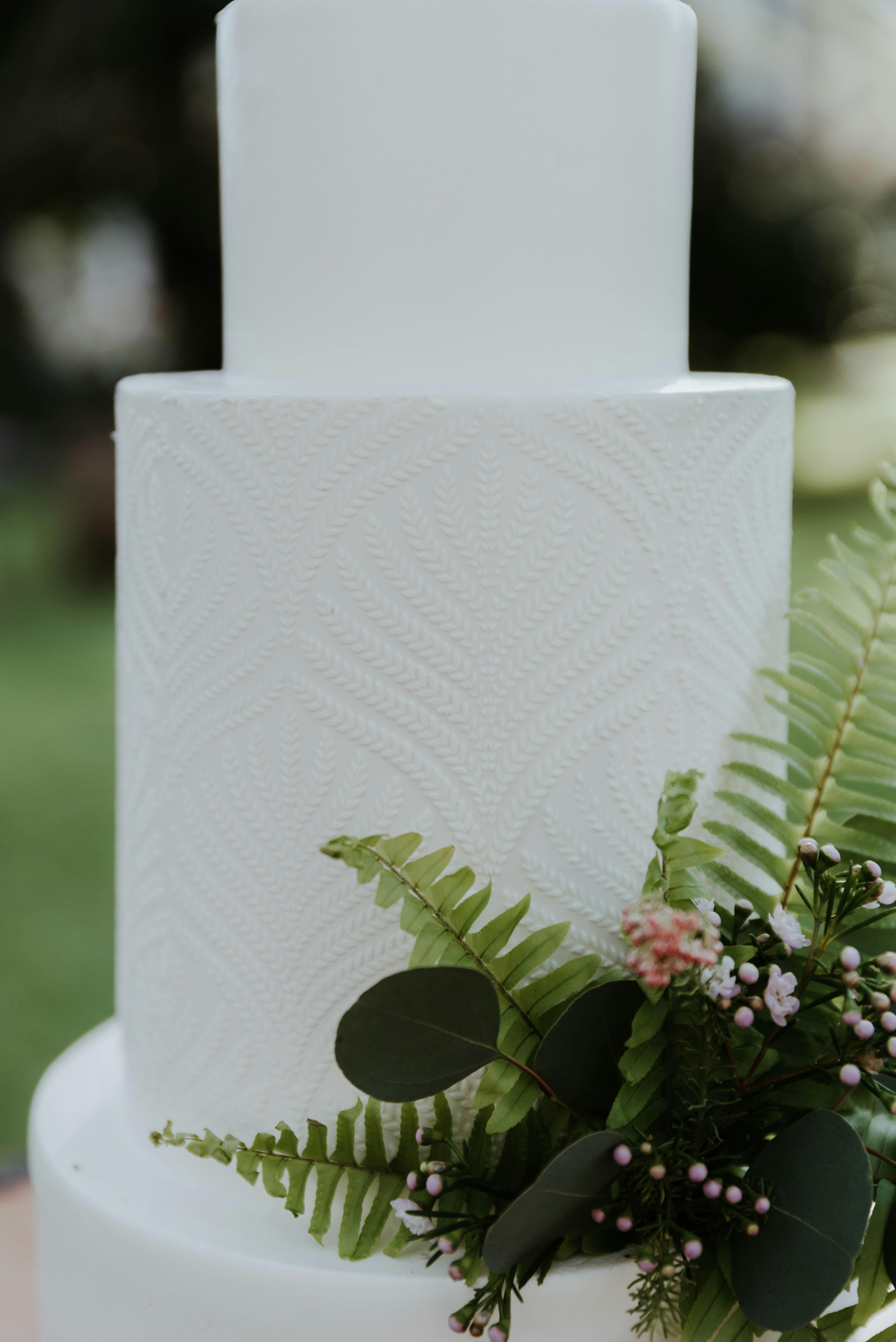 A minimalist white wedding cake adorned with green leaves and pink flowers, perfect for a sophisticated celebration.