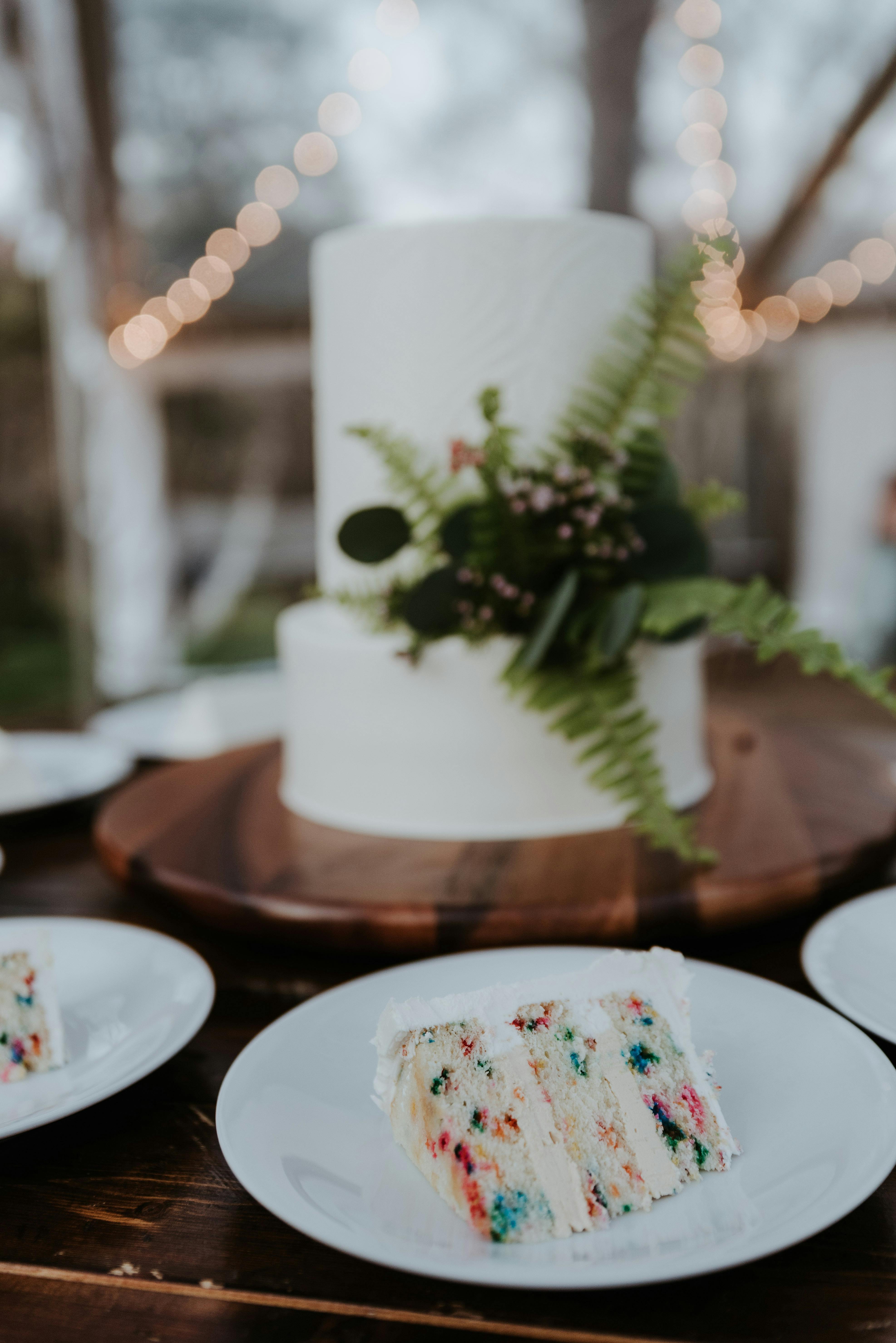 Beautiful white wedding cake with floral decorations and cake slice on plate outdoors.