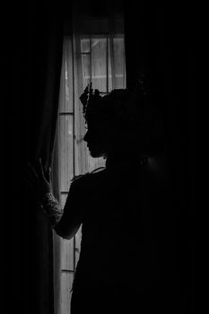 Dark silhouette of a person in traditional attire near a window.