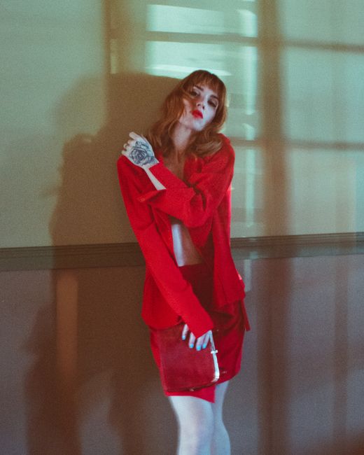 Stylish woman posing in red attire with hand tattoo in dramatic lighting.