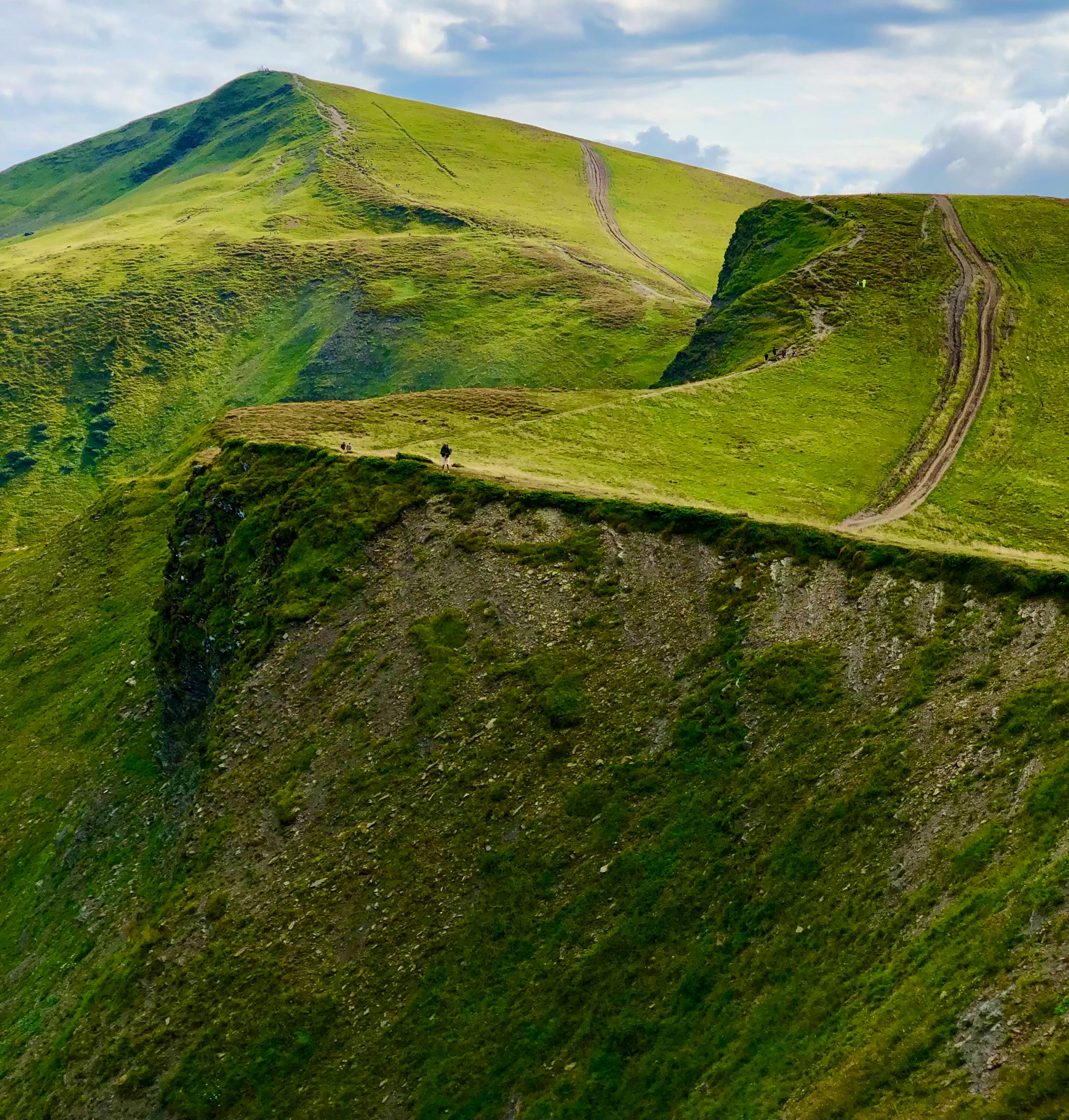 A breathtaking aerial view of expansive green hills and towering cliffs under a cloudy sky.