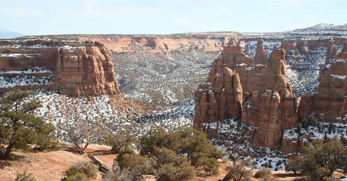 Breathtaking aerial view of Colorado's red rock canyons with snow-dusted landscape and clear blue sky.