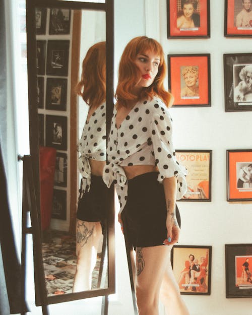A Woman in Polka Dots Top and Black Shorts Standing Near the Mirror