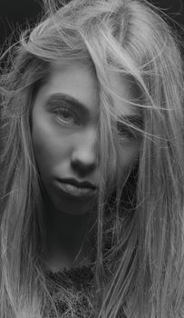 Close-up black and white portrait of a young woman with intense gaze and flowing hair.