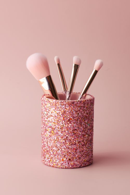 Free Pink glitter brush holder with makeup tools on a pink background, ideal for beauty product promotion. Stock Photo