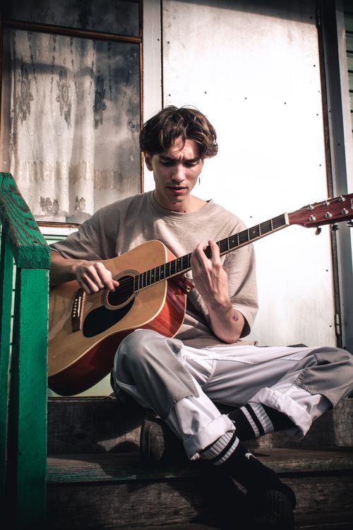 Free A young man sitting on stairs playing a guitar outdoors, showcasing a musical moment. Stock Photo