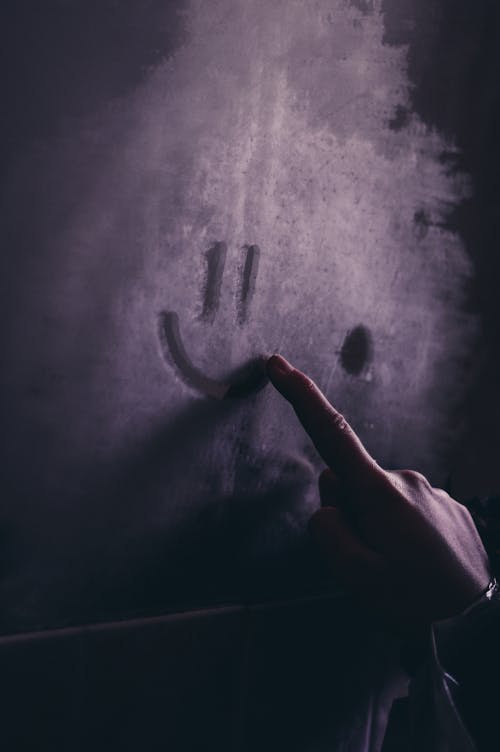 Hand Drawing a Smiley Face on a Dusty Glass 