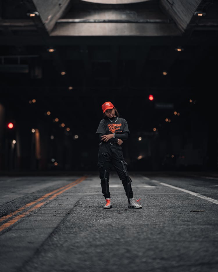 Teenage Girl In Black Outfit And Red Cap Standing On Road 