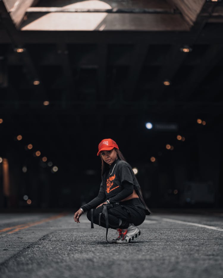 Teenage Girl In Black Street-wear And Red Cap Crouching On Road