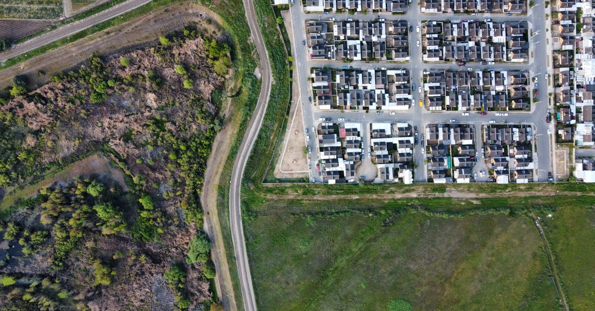 Drone view of a residential neighborhood alongside a natural landscape, showcasing urban and rural contrast.